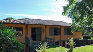 A two-story building with a tiled roof, a wooden porch, and a small garden with potted plants.