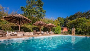 Una piscina cristalina con sillas de descanso y zonas a la sombra.
