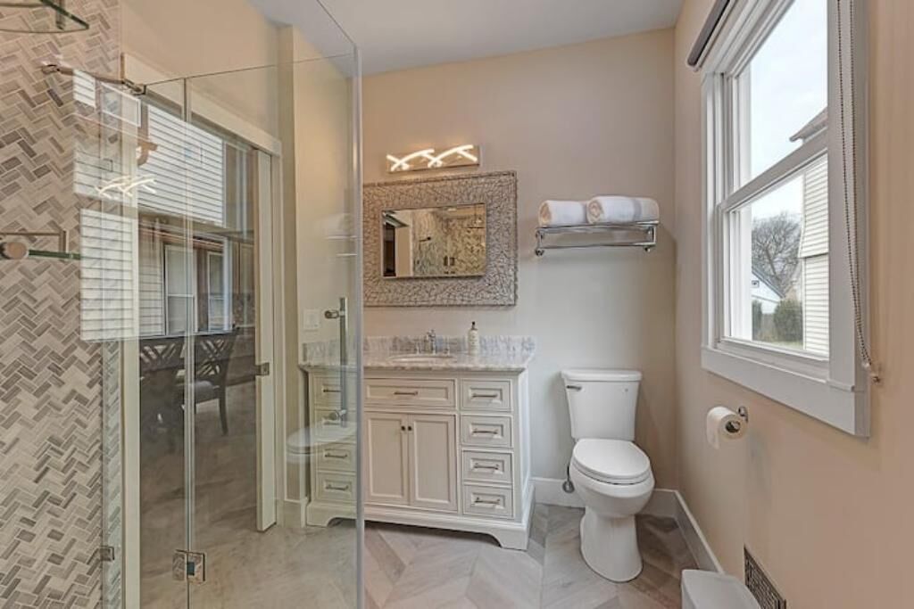 A bathroom with a glass shower enclosure, a white toilet, a vanity with drawers, and a mirror above the sink.