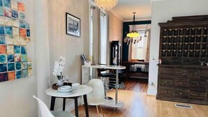Un comedor con una mesa redonda, dos sillas blancas, una araña y piso de madera.