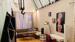 Un espacio habitable compacto con un sofá, una pequeña mesa de centro, un escritorio con una silla y un cuadro grande en la pared.