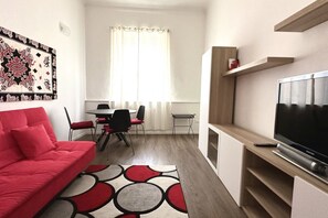 A modern living room with a red sofa, a dining area with a table and chairs, a TV on a wooden stand, and a patterned rug. - A34 - Ancona, delightful two-room apartment in the centre (Ancona)