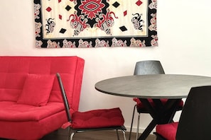 Een kamer met een rode bank, een ronde tafel en een behang met een patroon.
