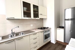 Een keuken met een roestvrijstalen koelkast, een gasfornuis, een dubbele spoelbak en lichte kastjes.