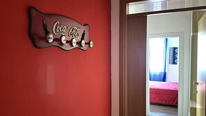 A red wall with a Coca-Cola sign and a door leading to a room with a bed and curtains. - A34 - Ancona, delightful two-room apartment in the centre (Ancona)