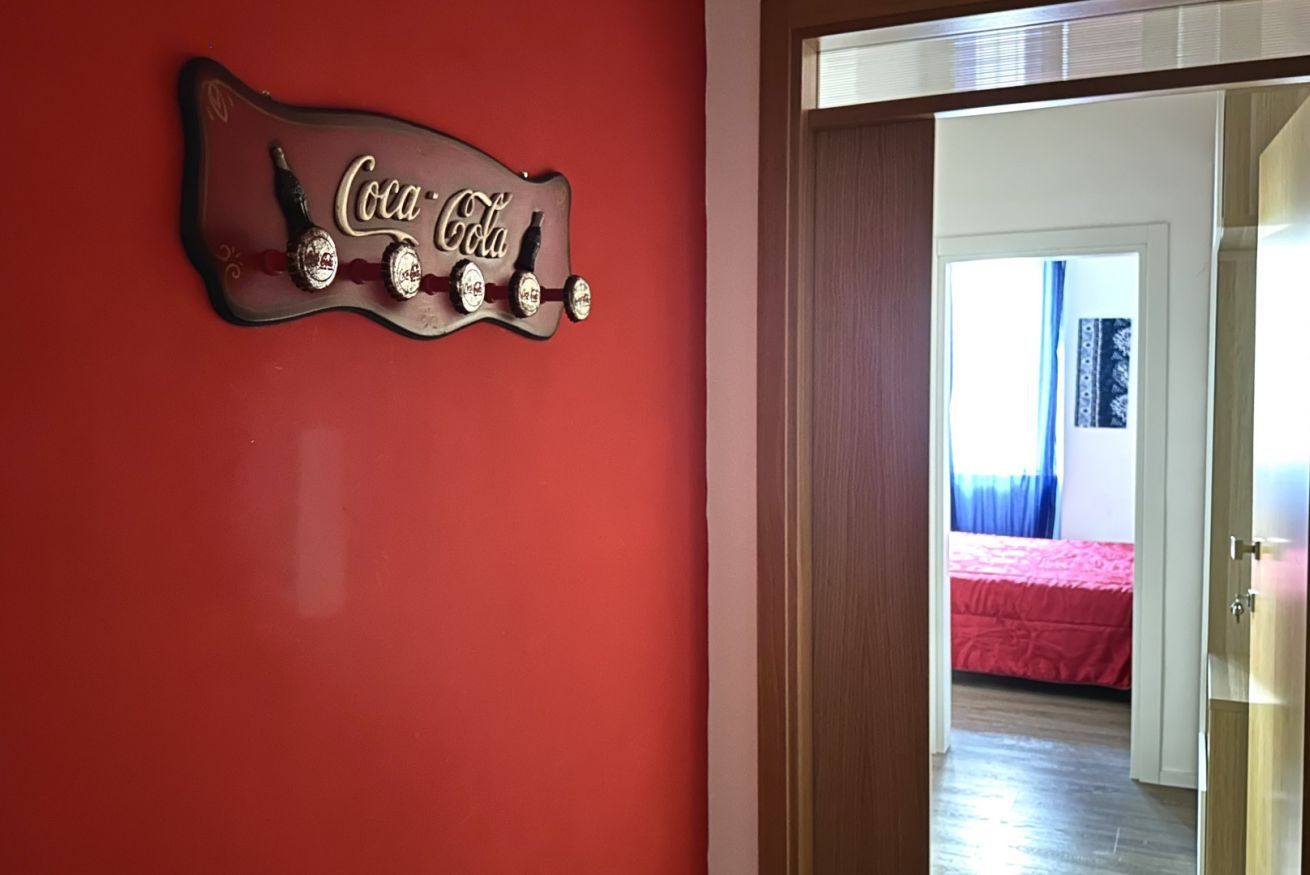 Pared roja con un letrero de Coca-Cola y una puerta que da a una habitación con cama y cortinas.