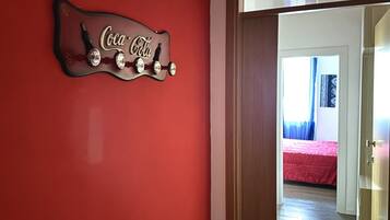 Pared roja con un letrero de Coca-Cola y una puerta que da a una habitación con cama y cortinas.