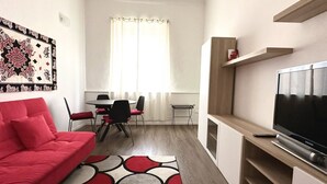 A modern living room with a red sofa, a dining area with a table and chairs, a TV on a wooden stand, and a patterned rug. - A34 - Ancona, delightful two-room apartment in the centre (Ancona)