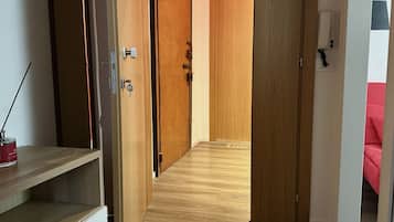 Un pasillo con puertas de madera, una pared blanca con un teléfono y un objeto rojo sobre una estantería.