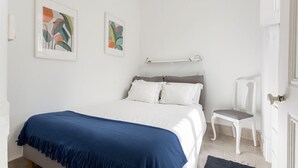 Une chambre à coucher avec un lit, une chaise et deux œuvres d’art encadrées accrochées au mur.