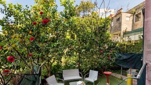 Un petit espace extérieur aménagé avec deux chaises et une table, entouré d’une végétation luxuriante et de plantes en fleurs.