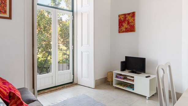 Une pièce avec une porte blanche, un téléviseur posé sur un meuble blanc et une bibliothèque.