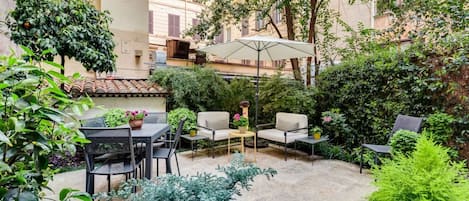 An outdoor patio area with a table and chairs, surrounded by potted plants and a large umbrella.