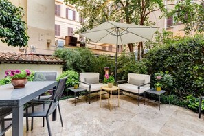 Ein möblierter Terrassenbereich mit Tisch, zwei Stühlen und einem großen Sonnenschirm.