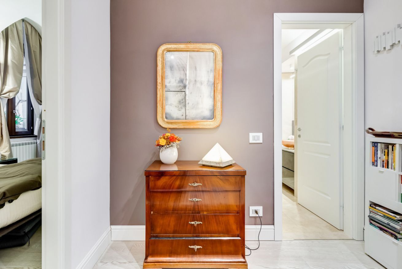A wooden dresser with drawers, a vase with flowers, and a framed picture on the wall.