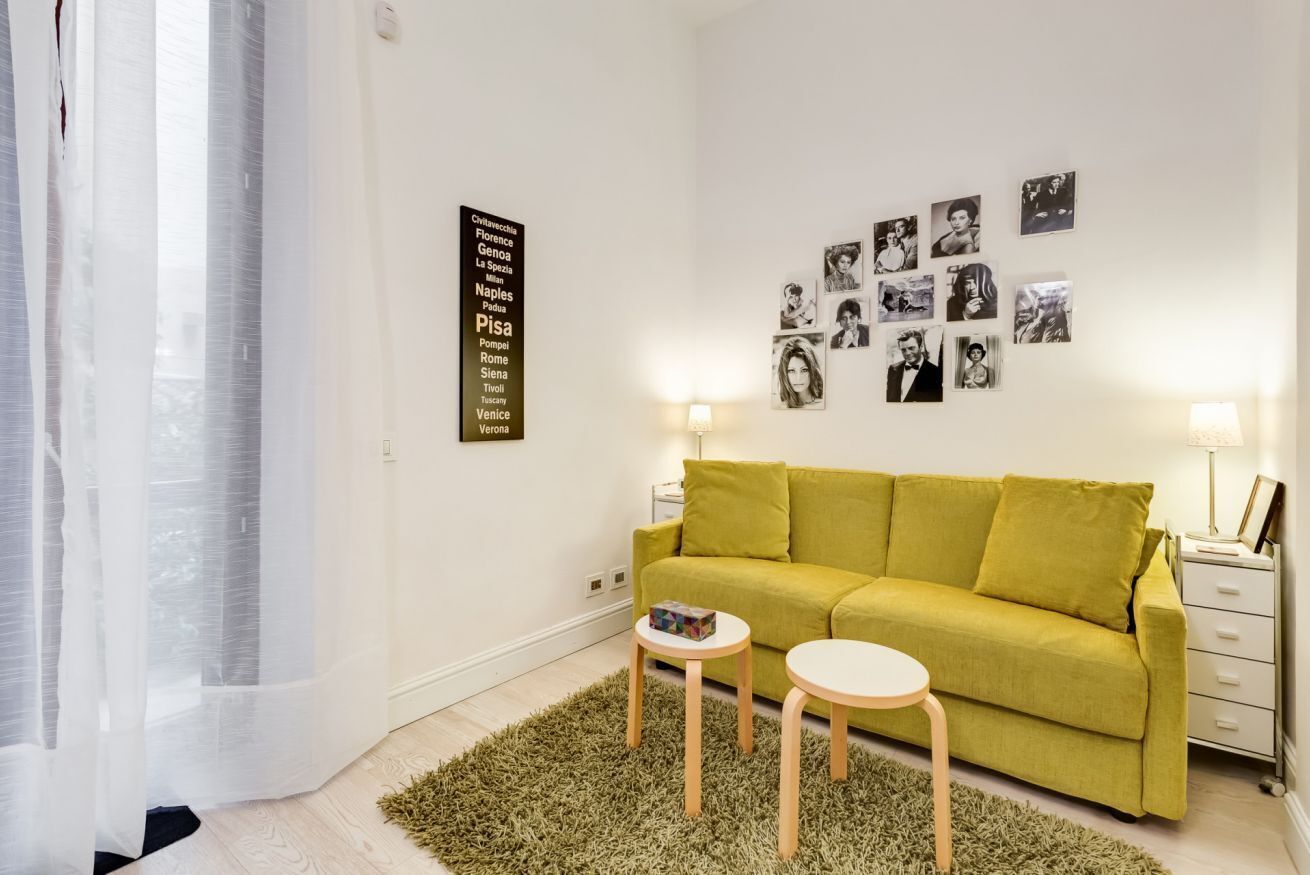 Un salon moderne avec un canapé vert, deux petites tables et un mur décoré de photographies en noir et blanc.
