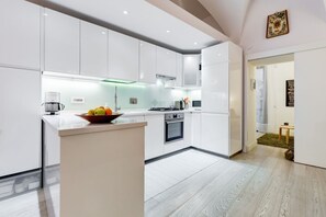 A modern kitchen with white cabinets, a central island with fruit, and a view into the adjacent living area.