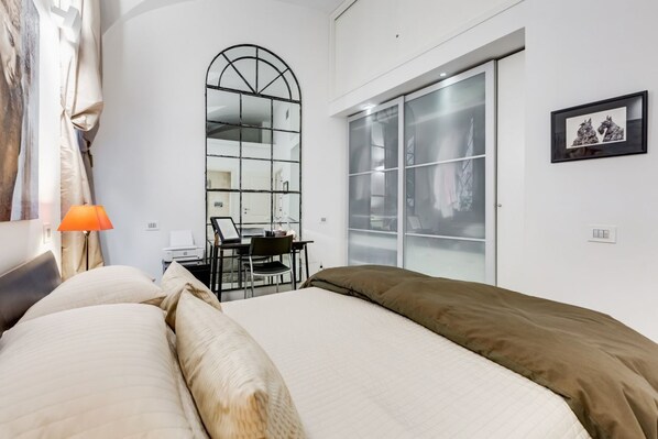 A bedroom with a bed, a desk, a chair, and a large window.