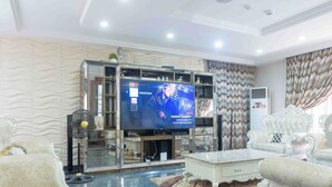 A modern living room with a large flat-screen TV, plush seating, and decorative elements. - 5 bed Home w/ Professional Chef, Strong Security, Daily Housekeeping (Abuja)