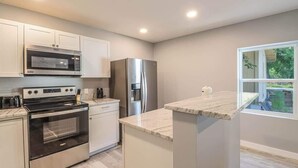 A modern kitchen with stainless steel appliances, white cabinetry, and a large window providing a view of the outdoors. - Cozy 2br/1ba Duplex Just Blocks From Downtown Biloxi, Beaches and Entertainment (Biloxi)