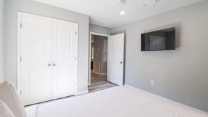 A bedroom with a bed, a TV, a wardrobe, and a door leading to another room. - Cozy 2br/1ba Duplex Just Blocks From Downtown Biloxi, Beaches and Entertainment (Biloxi)