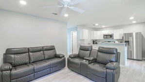 A modern living room with two leather sofas, a ceiling fan, and a kitchen in the background. - Cozy 2br/1ba Duplex Just Blocks From Downtown Biloxi, Beaches and Entertainment (Biloxi)