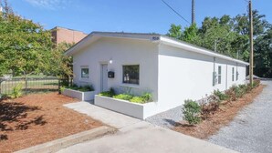 Un edificio blanco de una sola planta con techo plano, un pequeño porche con macetas y un buzón a la vista.
