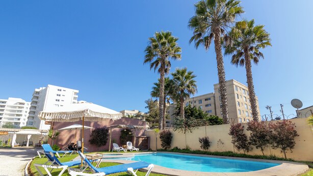 A swimming pool with lounge chairs, palm trees, and a building in the background. - Cabañas de la Costa (La Serena)