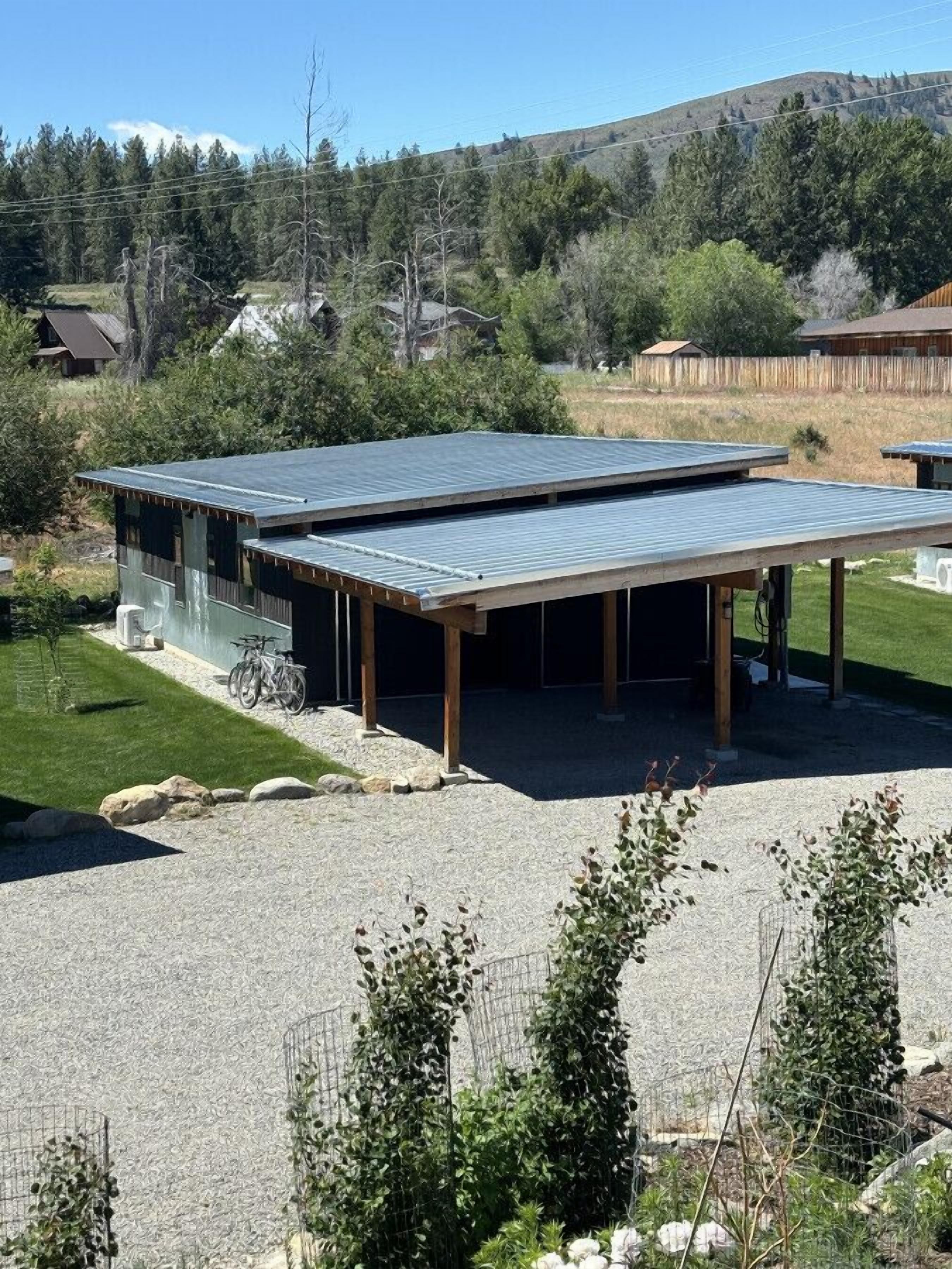 A modern building with a metal roof and wooden beams, surrounded by a well-maintained lawn and gravel driveway.