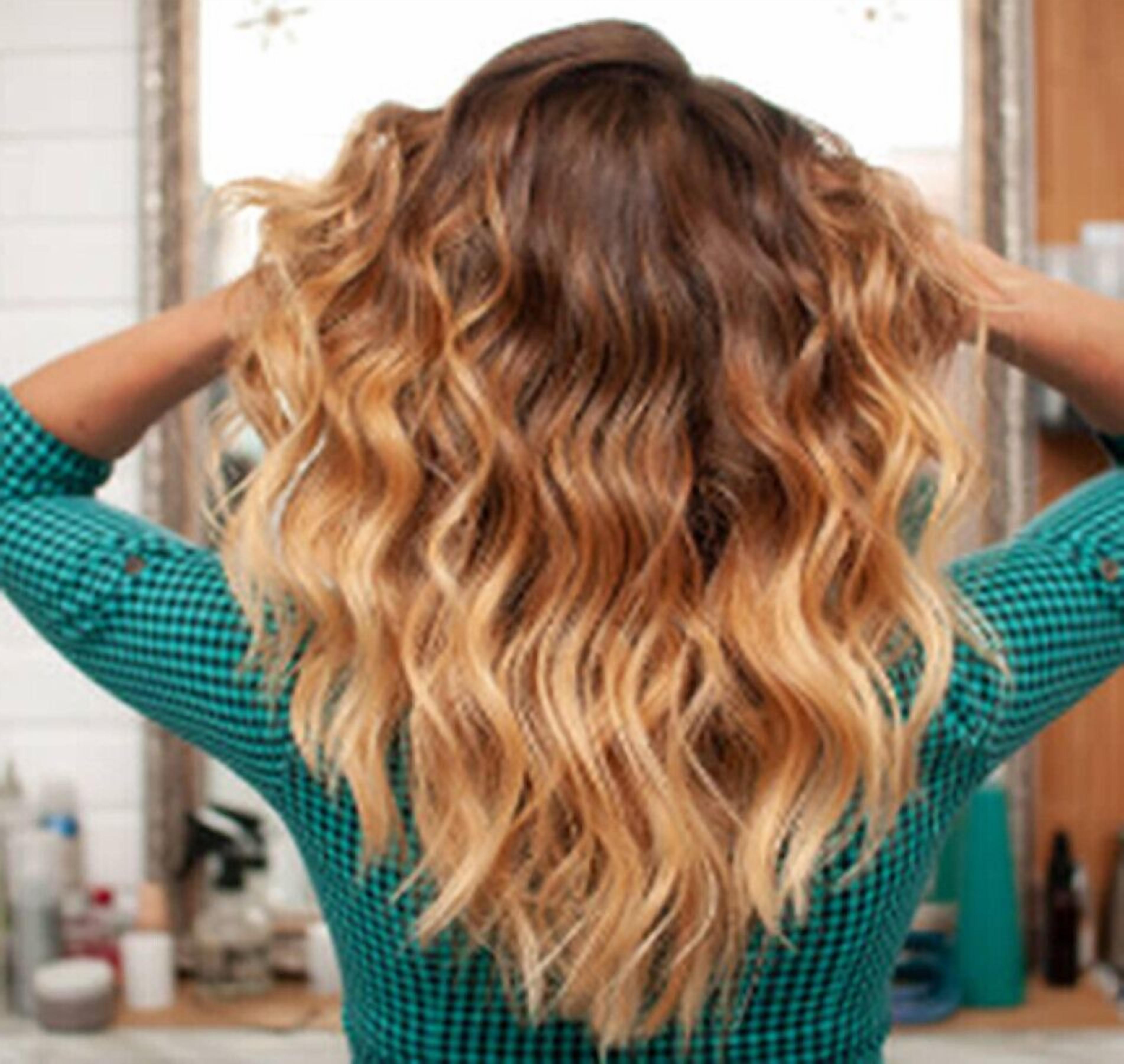Une personne aux longs cheveux ondulés, portant une chemise à carreaux.