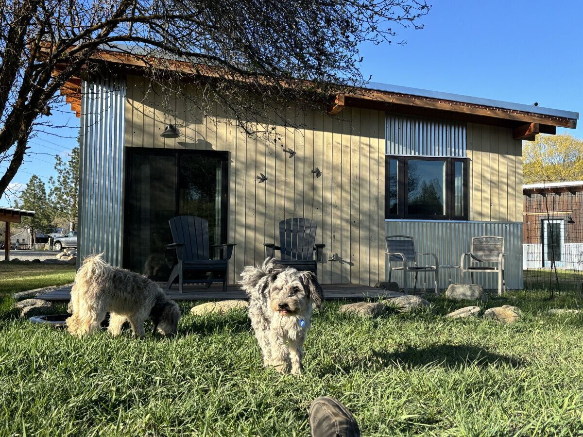 A rustic building with a large glass door, outdoor seating, and a grassy yard.