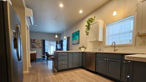 A modern kitchen with dark cabinets, a wooden floor, pendant lighting, and a window with a view. - Sunflower Resort Susan Cabin is in the ultra-quiet Winthrop South community, with a 10 minute walk to downtown & on the pedestrian trail. (Winthrop)