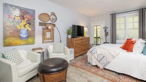 A well-lit room with a bed, a white sofa, a wicker chair, a TV, and a painting on the wall. - Gypsy Soul, Free Parking and Steps to Downtown Charm (Eureka Springs)