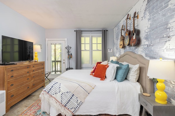A bedroom with a bed, a dresser, a TV, and guitars on the wall.