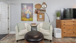 A living room with a sofa, ottoman, TV, and decorative items on the wall. - Gypsy Soul, Free Parking and Steps to Downtown Charm (Eureka Springs)