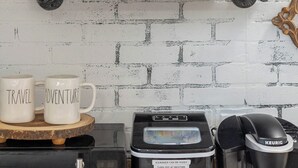 A kitchen with a white brick wall, a wooden shelf with a 'Welcome' sign, and a coffee maker on the counter. - Gypsy Rose: Free Parking and Steps to Downtown Charm (Eureka Springs)
