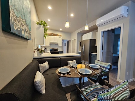 A modern kitchen with white cabinets, a central island, and a dining area with a round table and chairs.