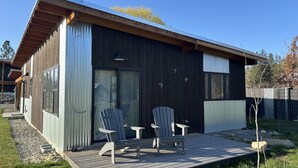 A modern house with a deck, two Adirondack chairs, and a large window.