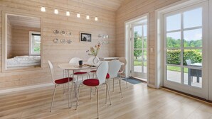 Un interior moderno con zona de comedor, cama y ventanas amplias que dan a zonas verdes.