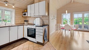 Una cocina moderna con armarios blancos, horno empotrado y microondas. Cuenta con un comedor con mesa y sillas, y amplias ventanas que ofrecen vistas al exterior.