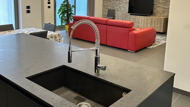 A modern kitchen with a central island, a red sofa, and a stone wall with a flat-screen TV. - Entire Apartment at the foot of Valpolicella! (Pescantina)