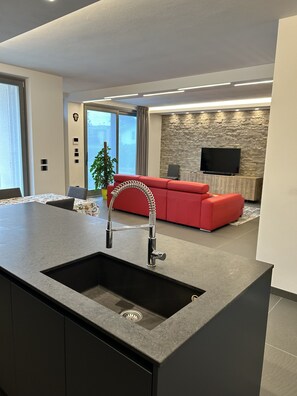 A modern kitchen with a central island, a red sofa, and a stone wall with a flat-screen TV. - Entire apartment at the foot of Valpolicella! (Pescantina)