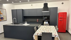 A modern kitchen with a central island, dark cabinetry, a red refrigerator, and a dining area with a floral tablecloth. - Entire Apartment at the foot of Valpolicella! (Pescantina)