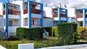 A multi-story residential building with balconies, a paved driveway, and well-maintained greenery.