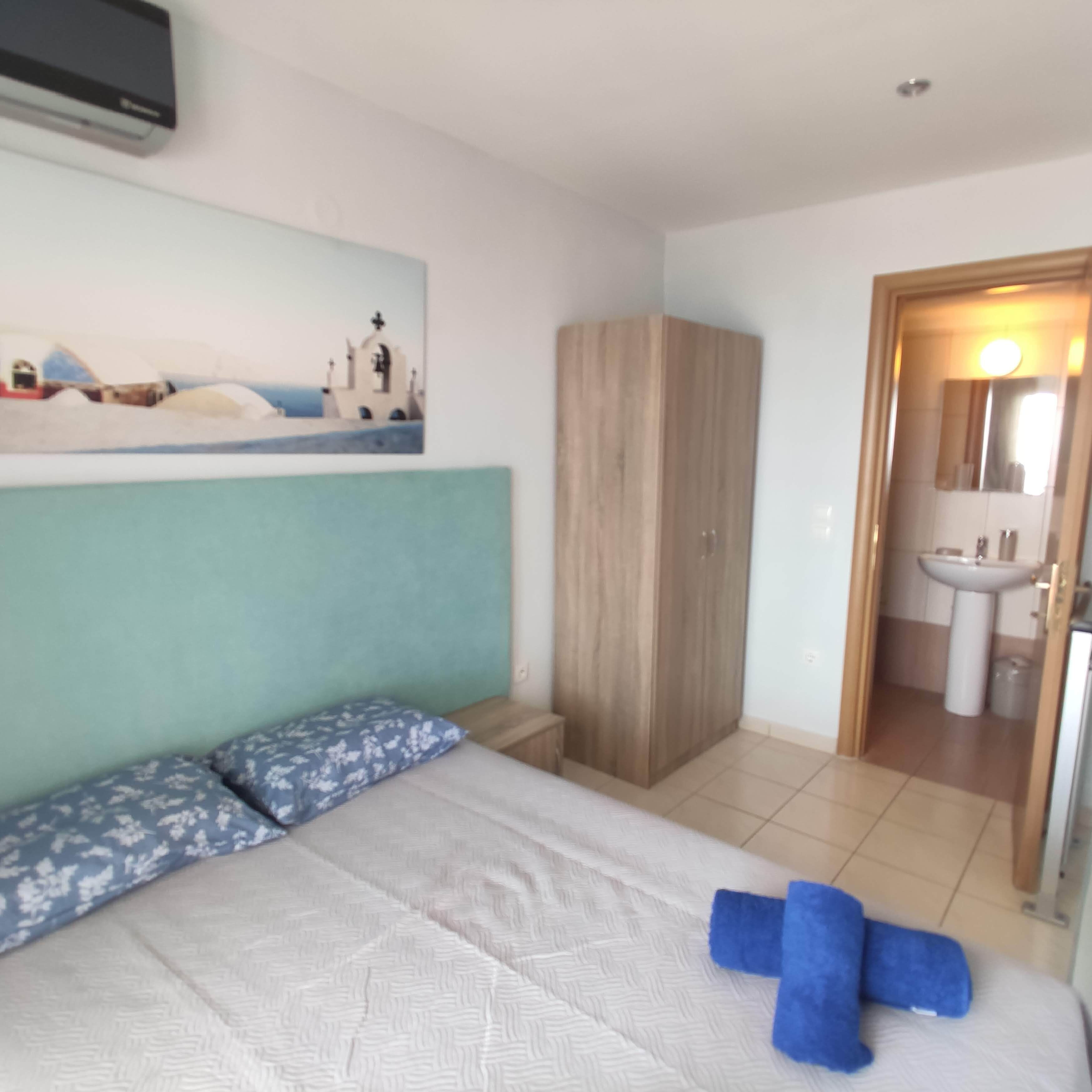Quarto com cama, guarda-roupa, banheiro com pia e espelho, e um quadro na parede.