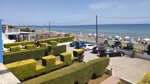 A coastal view with neatly trimmed hedges, a parking area, and beach umbrellas.