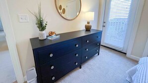 A bedroom with a dark blue dresser, a round mirror, a small plant, and a lamp. - Belmont 2BR - Minutes to CaroMont | 14+ Nights (Belmont)