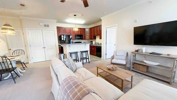 A modern living room with a sofa, coffee table, and TV. There is a kitchen in the background with wooden cabinets and a microwave. - Belmont 2BR - Minutes to CaroMont | 14+ Nights (Belmont)