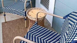 A small outdoor seating area with two wicker chairs and a round table, against a light blue wall and a white door. - Belmont 2BR - Minutes to CaroMont | 14+ Nights (Belmont)