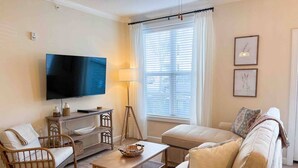 A living room with a flat-screen TV, a sofa, a chair, a coffee table, and a lamp. - Belmont 2BR - Minutes to CaroMont | 14+ Nights (Belmont)